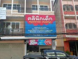 ป้ายสินค้าคลีนิกเด็กสีชมพูและฟ้าติดตั้งบนร้านค้าทำเลชั้นสองของอาคารพาณิชย์สี่ชั้นในพื้นที่ชุมชน