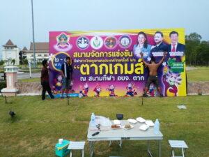 ป้ายโครงการสนามจัดการแข่งขันกีฬาไทยฟุตบอลระดับประเทศปีการศึกษา 2566 ในสนามกีฬา อบจ.ตาก พร้อมตารางอาหารและเก้าอี้นั่งในพื้นหญ้าสีเขียว