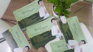หนังสือและโบรชัวร์สีเขียวอ่อนที่มีรูปคนชายวัยกลางคนใส่เสื้อสีชมพู พร้อมต้นไม้สีเขียวในกระถาดสีขาว