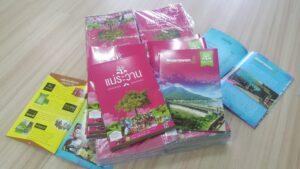 กองแพมเพลตและแผ่นพับท่องเที่ยวแม่ระวาน สีชมพูและสีฟ้า วางบนพื้นไม้