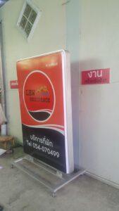ป้ายโฆษณา LEW Residence สีแดงและดำตั้งอยู่หน้าผนังสีเหลือง พร้อมข้อมูลการติดต่อและหมายเลขโทรศัพท์