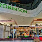 ป้ายสีเขียวชื่อ Robinson บนเพดานห้างสรรพสินค้า พร้อมร้านค้า Happy Market ด้านล่าง