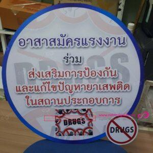 ป้ายวงกลมสีน้ำเงินและสีขาวแสดงข้อความภาษาไทยเกี่ยวกับสมัครสมาชิกอาสาสมัครแนวต้านยาเสพติด พร้อมสัญลักษณ์ห้ามยาเสพติด