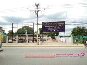 ป้ายโครงการก่อสร้างสถาบันการศึกษาขนาดใหญ่ในประเทศไทย ติดตั้งบนรั้วคอนกรีตสีขาว พร้อมลวดสายไฟและเสาไฟฟ้า