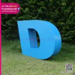 ตัวอักษรสีน้ำเงินสามมิติขนาดใหญ่ "d" ยืนอยู่บนสนามหญ้าที่มีข้อความโฆษณาและรหัส QR ผู้ติดต่อในบริเวณชายแดน