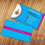 นามบัตรสีฟ้าและสีชมพูของรุ่งมูลม มีโลโก้วัดสีทองและข้อมูลติดต่อบนพื้นไม้