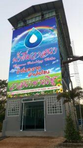 ป้ายโฆษณาขนาดใหญ่สำหรับธุรกิจจำหน่ายน้ำดื่มบริสุทธิ์ ติดตั้งบนตึกปลายปีที่มีสัญลักษณ์หยดน้ำสีฟ้าและพื้นหลังท้องฟ้าสีสันสดใส