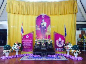 ห้องประดับตกแต่งด้วยผ้าสีเหลืองและจัดสมัยสักการบูชา มีพระบรรจุศพและดอกไม้สีขาวสีชมพู พร้อมธงชาติไทย