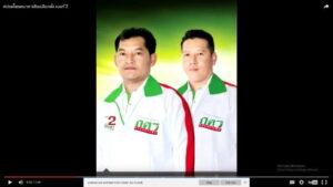 สองชายคนไทยสวมชุดสีขาวมีปกเขียวและเนคไทสีแดง โลโก้ DAZ สีเขียวและแดงบนหน้าอก พื้นหลังไล่สีเขียวและเหลือง