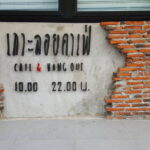 ป้ายสีขาวบนผนังอิฐสีแดง แสดงชื่อร้านและเวลาเปิด-ปิด