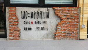 ป้ายสีขาวบนผนังอิฐสีแดง แสดงชื่อร้านและเวลาเปิด-ปิด